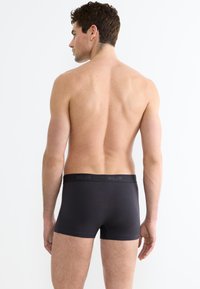 Boxer aderenti neri realizzati in tessuto liscio con una cintura elasticizzata marchiata. Il design è attillato e presenta uno stile semplice e minimalista.