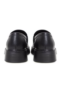Paire de mocassins en cuir noir avec semelles épaisses rainurées, vus de dos sur fond blanc.