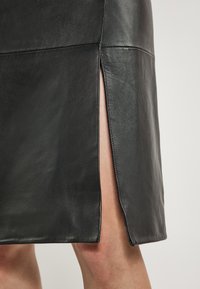 Mustat nahkahameet, joissa on sivuaukko ja sauma-yksityiskohtia. Sileä pinta, tiukka muotoilu ja minimalistinen design. Sopii monenlaisiin tilaisuuksiin.