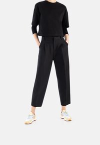 Schwarzes, kurzes T-Shirt, lockere schwarze Hose mit Falten und wei�ße Sneakers mit gelben und blauen Akzenten. Glatte Textur, lässiges Design.