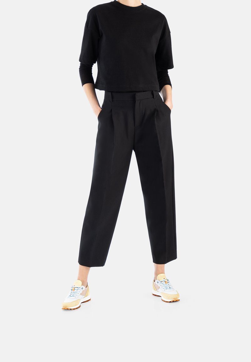 Schwarzes, kurzes T-Shirt, lockere schwarze Hose mit Falten und weiße Sneakers mit gelben und blauen Akzenten. Glatte Textur, lässiges Design.