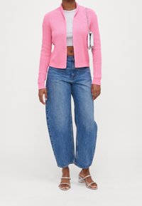 Růžový žebrovaný pletený kardigan, šedý krátký top, široké modré džíny a stříbrné sandály na podpatku s masivním páskem a průhledným blokovým podpatkem.