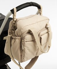 Borsa per pannolini imbottita beige con più tasche esterne, tracolla regolabile e doppio manico superiore. Texture liscia e design leggero.