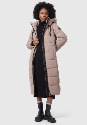 Pitkä beige puhvitakki hupulla, mustalla vetoketjulla ja yksityiskohdilla, jossa on paljetti kuosi ja sivutaskut, pukeutuneena mustan ribattu mekko päällä.