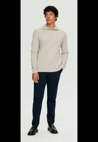 Ανοιχτό γκρι φούτερ με φερμουάρ και μακριά μανίκια σε συνδυασμό με σκούρες μπλε παντελόνες. Το σύνολο ολοκληρώνεται με μαύρα παπούτσια.