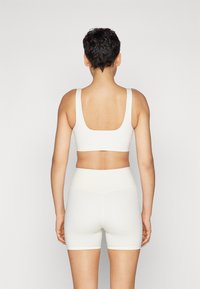 Top crop atlético branco com alças largas e decote quadrado, emparelhado com calções de cintura alta a condizer, ambos feitos de um material elástico e suave.