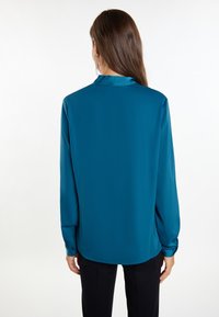 Bluzka z satyny w kolorze teal, z długimi rękawami, kołnierzem z tyłu i mankietami na guziki, zaprezentowana z tyłu, charakteryzująca się gładką i lśniącą fakturą.