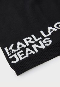 Svart strikket stoff med teksten "KARL LAGERFELD JEANS" i fremtredende hvite bokstaver, med ribbestruktur langs kanten.