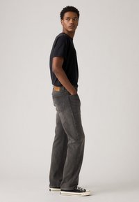 Black short-sleeve t-shirt, gray straight-leg jeans with a light wash, back pocket detailing, and black sneakers with white soles.