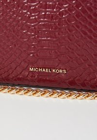 Burgundy faux snake skin handbag with a gold chain strap and embossed "MICHAEL KORS" logo at the front. Textured surface with glossy finish.