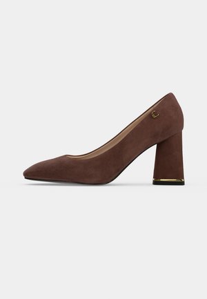 Chaussure à talon haut en daim marron avec talon bloc, accent doré à la base du talon et petit emblème doré sur le côté extérieur près de la cheville.