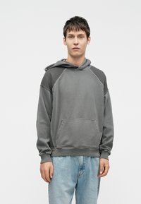 Gray hooded sweatshirt featuring a relaxed fit, raglan sleeves, and a front pocket, paired with light blue jeans. Smooth texture, minimal design.
