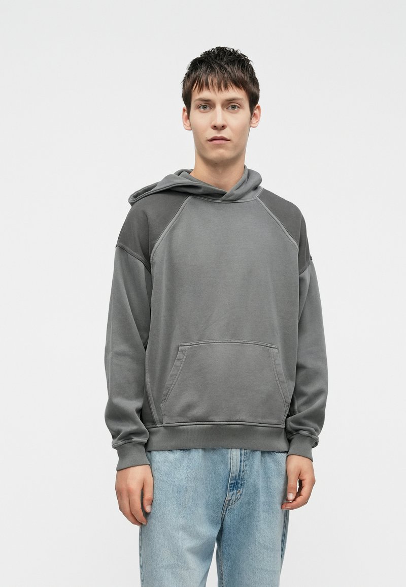 Gray hooded sweatshirt featuring a relaxed fit, raglan sleeves, and a front pocket, paired with light blue jeans. Smooth texture, minimal design.