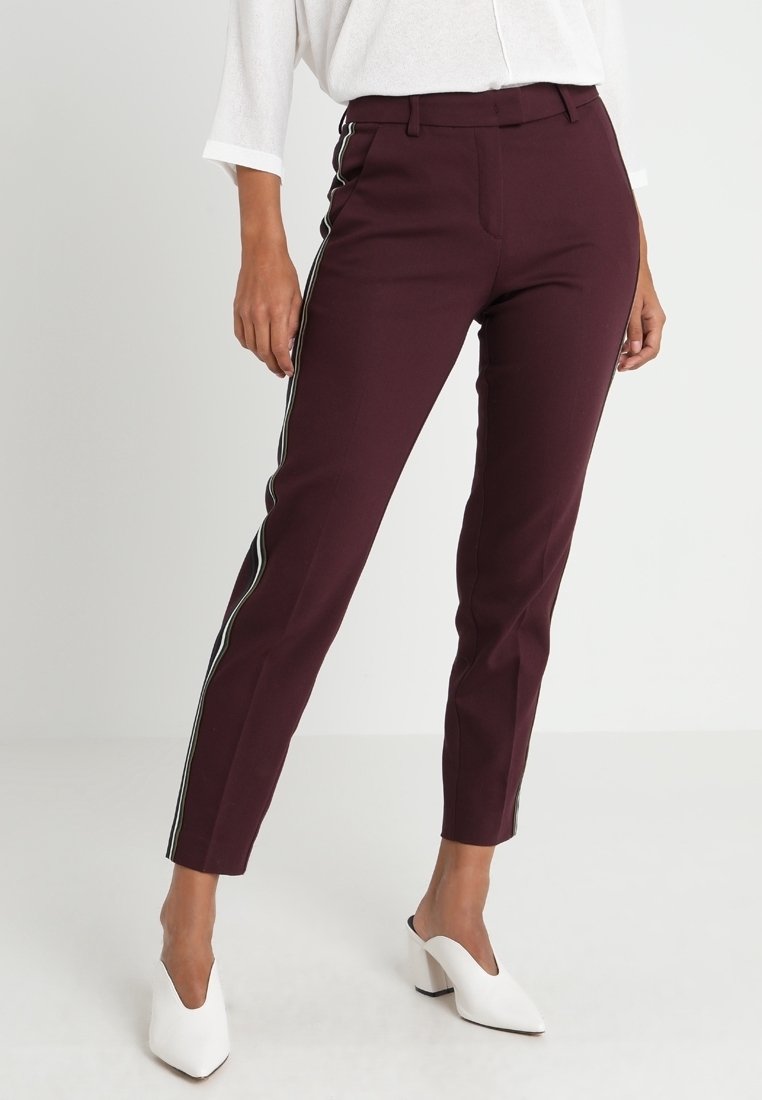 Burgundowe spodnie na miarę z białymi paskami po bokach, slim fit, wysoki stan, wykonane z gładkiego materiału, w parze z białymi klapkami na obcasie.