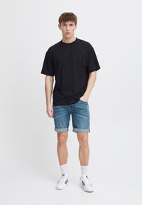 Crna pamučna majica kratkih rukava, uparena sa svijetlim plavim trapericama, i bijelim tenisicama s crnim detaljima. Jednostavan, ležeran outfit.