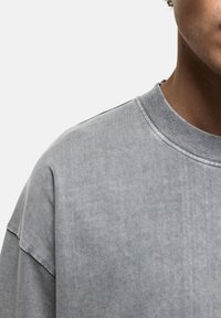 Szary bawełnowy sweatshirt z okrągłym dekoltem, charakteryzujący się teksturowanym wykończeniem i luźnym krojem, prezentujący subtelne cieniowanie oraz minimalne detale szycia.
