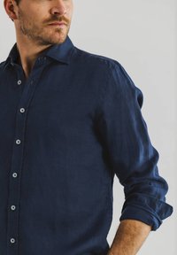 Marineblauwe linnen shirt met button-down kraag, voorzien van lichte knopen en opgerolde mouwen, die een geweven stof laat zien.