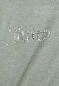 Světlounce zelená bavlněná látka s jiskřivým logem "Juicy" zdobeným kamínky. Hladká textura, ležérní design, lehký materiál.