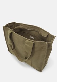 Torebka z płótna w oliwkowym kolorze z dwoma uchwytami i zamykaną na zamek wewnętrzną kieszenią oznaczoną napisem "ZIGN" na białym tle.