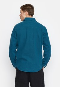 Teal overhemd met lange mouwen, een gespreide kraag en een gebogen zoom. Getextureerde stof met een subtiel weefpatroon.