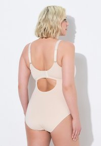 Beige badpak met verstelbare bandjes, open rugdetail, gladde textuur en elastische stof voor comfort en ondersteuning.