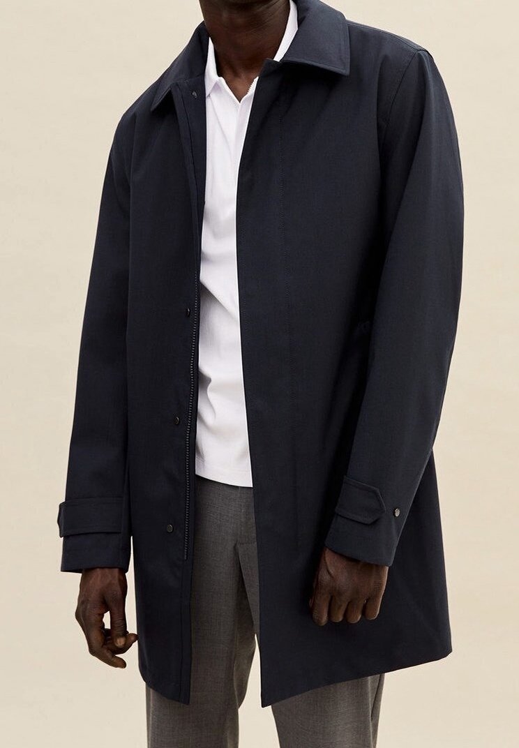 Cappotto impermeabile blu navy con colletto appuntito, polsini con bottone e chiusura frontale con snap. Presenta una vestibilità dritta e un design elegante.