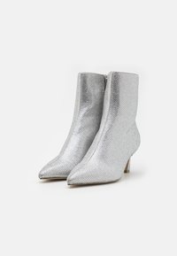 Botas de tobillo plateadas con una superficie brillante y texturizada, punta afilada y un pequeño tacón cuadrado. Presenta un cierre de cremallera lateral.