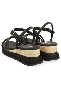 Sandalias negras de tiras con una plantilla de yute trenzado, plataforma de goma negra y suela texturizada. Incluye un hebilla ajustable en el tobillo.