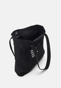 Černá taška na rameno vyrobená z udržitelné bavlny, s textem "REDUCE REUSE RECYCLE" v bílé barvě. Jednoduchý design se sturdy rukojeťmi.