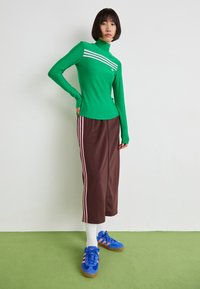 Πράσινη μπλούζα με μακριά μανίκια και ροζ ρίγες, καφέ φούστα μεσαίου μήκους με ροζ πλαϊνές ρίγες, λευκές κάλτσες και μπλε παπούτσια. Λείες και εφαρμοστές υφές.