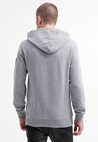 Felpa grigia realizzata in tessuto morbido, con un grande cappuccio, maniche lunghe e orlo a coste. Design semplice senza motivi o dettagli.