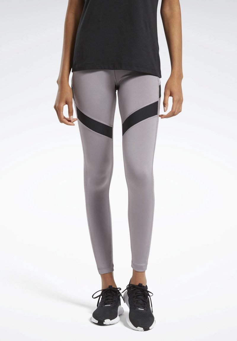 Leggings grigi chiaro con strisce diagonali nere, realizzati in materiale elasticizzato. Abbinati a scarpe da ginnastica nere, con un design testurizzato.