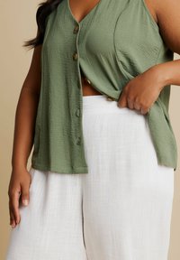 Olivgrön, ärmlös knapplöst topp med strukturerad yta, i kombination med vita, löst sittande, lätta byxor med subtila linjer.
