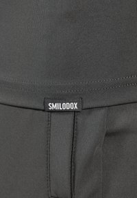 Graue Sportleggings aus glattem Stoff verfügen über einen Bund und ein Etikett mit "SMILODOX", das an der Seitennaht aufgenäht ist.