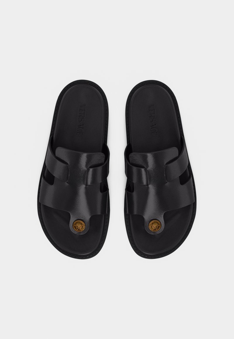 Black leather slide sandals with wide straps, embossed "Versace" insoles, and gold Medusa emblem on toe section, shown from above.