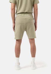 Pantaloni corti verdi con elastico in vita e tasca posteriore, caratterizzati da una consistenza morbida e una vestibilità comoda. Indossati con sneakers bianche e calze.