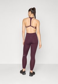 Bordeaux sportbh met een ontwerp van achterbanden en hooggetailleerde legging in dezelfde kleur. Zwarte sportschoenen met een gestructureerd oppervlak.
