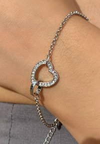 Bracelet en argent avec un charm en forme de cœur orné de cristaux transparents. Les maillons de la chaîne sont lisses, reflétant la lumière avec une finition polie.
