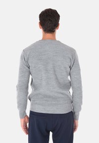 Maglione grigio a maglia con scollatura rotonda e maniche lunghe, caratterizzato da un motivo testurizzato, abbinato a pantaloni scuri, visto da dietro.