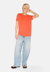 Orange short-sleeve t-shirt paired with light blue wide-leg jeans and black sandals, featuring a relaxed fit and soft texture.