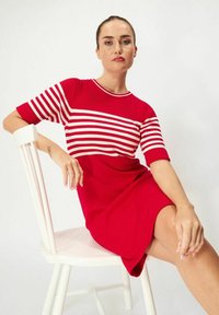 Punainen ja valkoinen raidallinen neulemekko, jossa on istuva yläosa ja levenevä hameosa. Lyhyet hihat, ribbikuvio ja sileä kangas hameen alaosassa.