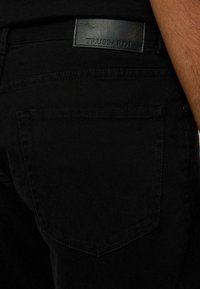 Jeans de mezclilla negra con una textura suave, que presentan una etiqueta con el logo de Trussardi en la parte trasera de la cinturilla y un diseño de bolsillo estándar.