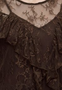 Tissu en dentelle marron foncé à motif floral et couches volantées, avec une section en résille transparente en haut ornée de fleurs brodées.