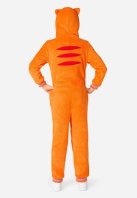 Oranžno plišasto enodelno oblačilo s kapuco, ki ima mačje ušesca. Rdeče črte na hrbtu in rebrasti manšeti v vijolični in roza barvi. Očitno je vidna bela obutev.