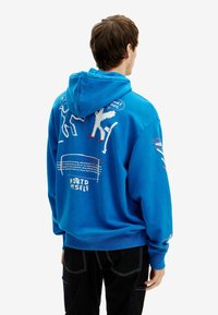 Modrá mikina s kapucí se šňůrkami, potištěnými obrázky na zádech a textem včetně "NOTED MYSELF." Měkký bavlněný materiál, pohodlný střih.