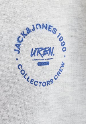 Camiseta de algodón gris con logo en círculo azul que lleva el texto "JACK & JONES 1990", "URBN" y "COLLECTORS CREW". Textura suave y diseño casual.