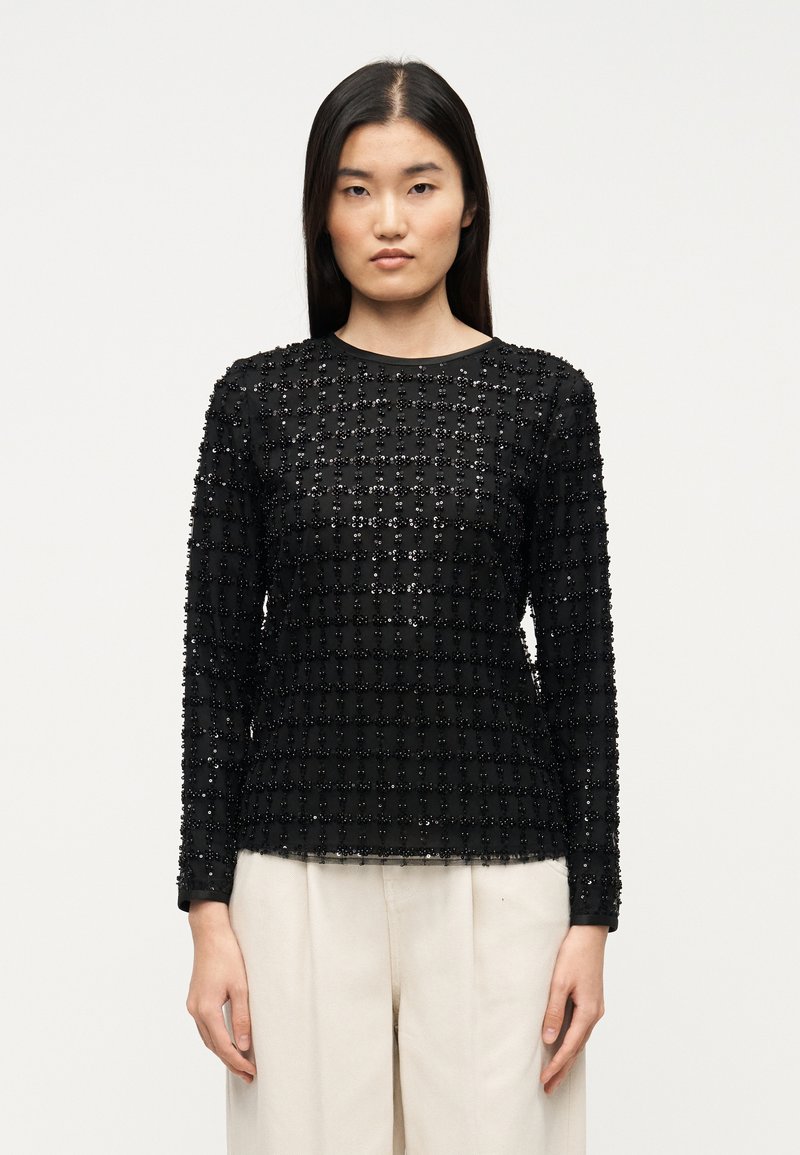 Μαύρο μακρυμάνικο τοπ με υφή υφάσματος που διαθέτει πλέγμα από παγιέτες, στρογγυλή λαιμόκοψη και εφαρμοστή σιλουέτα. Συνδυασμένο με ανοιχτόχρωμο παντελόνι.