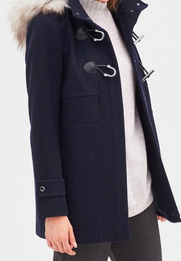 Navy blue winter coat with fur-trimmed hood, toggle closures, cuff button detail, worn over light gray sweater and dark pants.