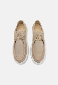 Beige gambersko med rund tå, med tonet søm og hvit gummisåle. Snøreløs design med tynne, matchende snører.