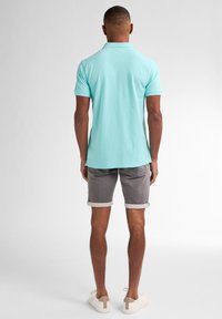 Polo shirt azzurro chiaro con maniche corte, abbinato a pantaloni corti grigi arrotolati e sneakers bianche con accenti beige. Visualizzazione dal retro.